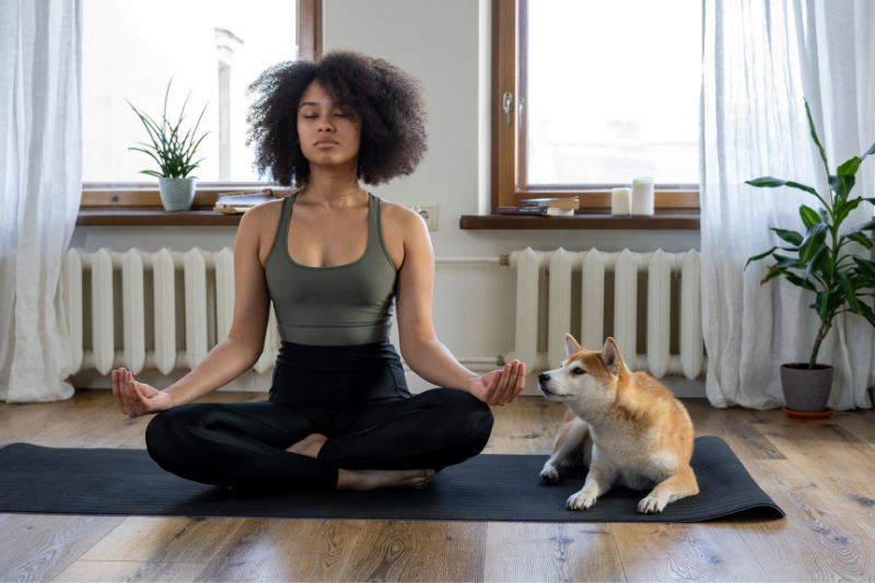women on yoga mat mediating with dog